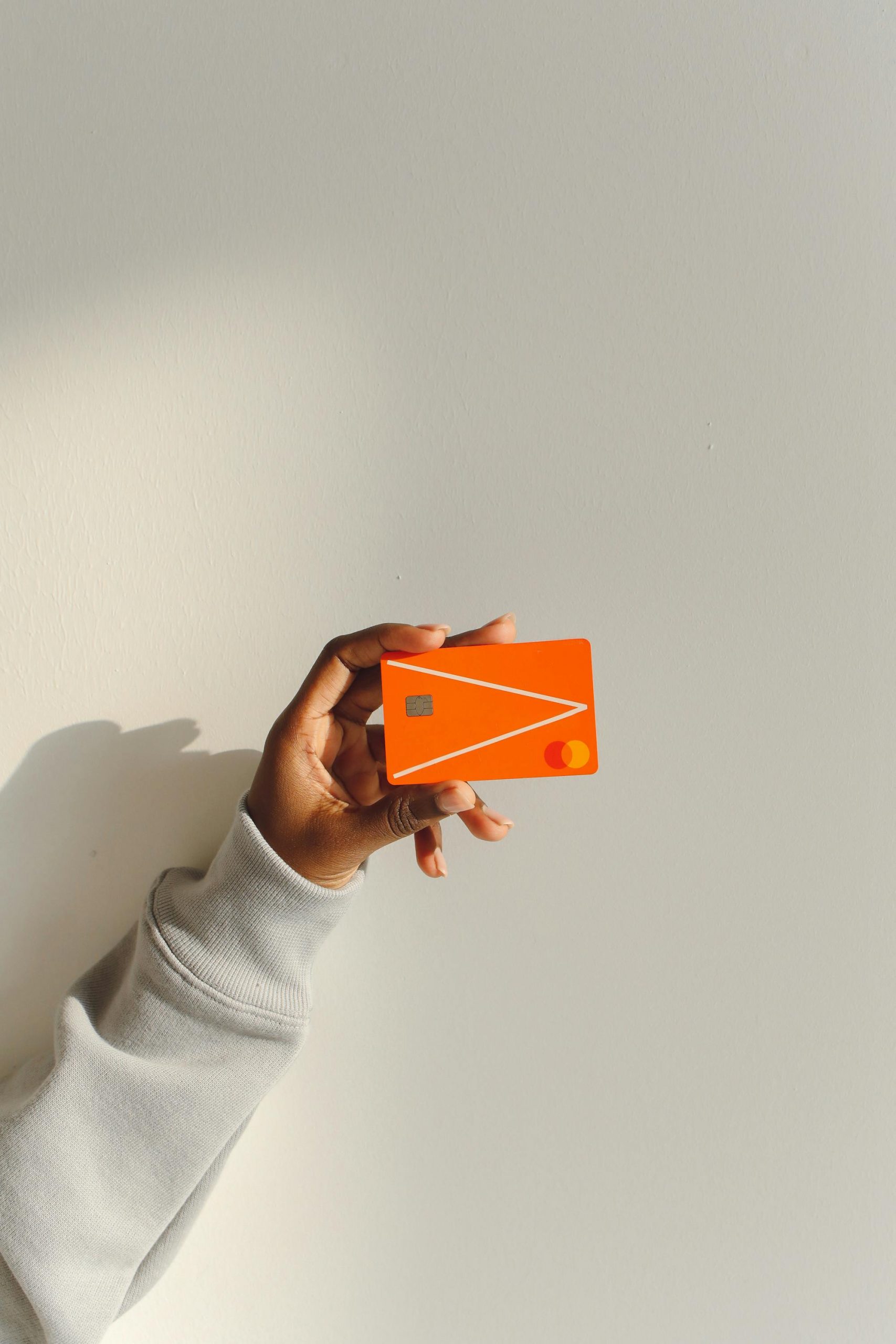 Close-up of a hand holding a bright orange debit card against a light background.
